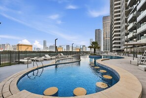 A rooftop pool with a circular design, surrounded by lounge chairs and a cityscape view. - Luxe JVC Studio with Skyline Views, Pool and Gym (Dubai)