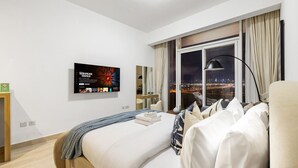 A hotel room with a bed, a TV mounted on the wall, a window with a city view, and a nightstand.