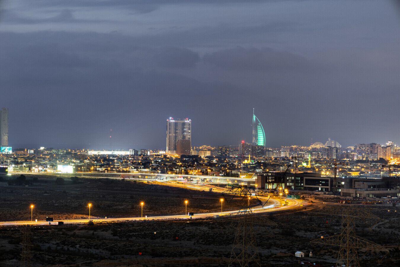 Ein Stadtbild bei Nacht mit beleuchteten Gebäuden, einem markanten, geschwungenen Wolkenkratzer und einer Autobahn mit Lichtern.