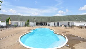 Une piscine entourée d’une terrasse, avec des espaces de détente en plein air, et un bâtiment doté d’un toit végétalisé en arrière-plan.