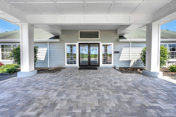 A covered entrance to a building with a herringbone-patterned walkway, double doors, and a small window above the doors.