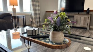 A glass-top coffee table with a tray holding a small potted plant and a stack of coasters. - Work + Relax + Play | 3BR Home w/ Ping Pong Table (Liverpool)