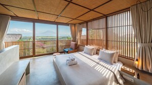 A spacious room with a large bed, a small table, and a chair, with a view of the landscape through large windows. - Mizu Homes (Lembongan Island)