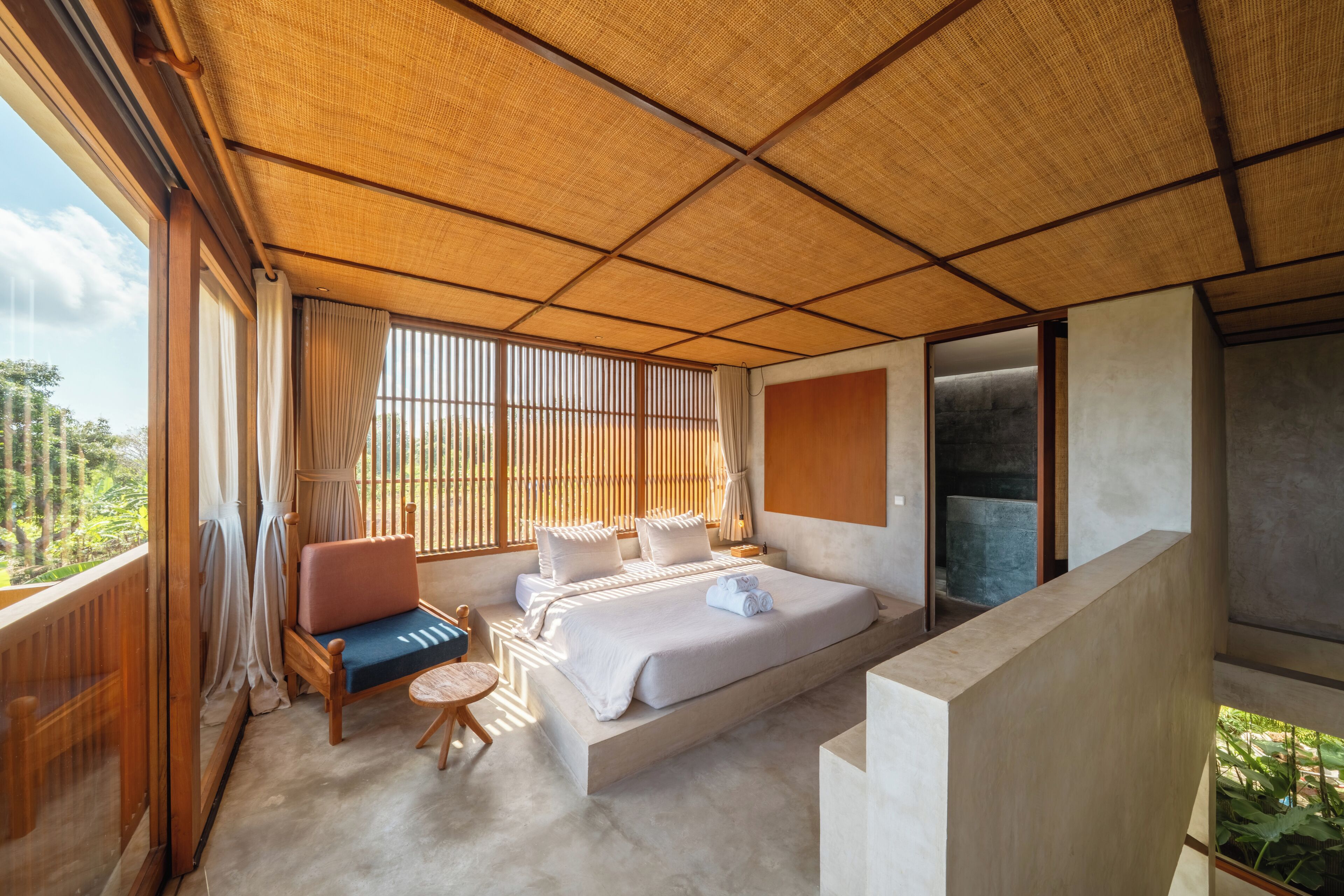 A bedroom with a large bed, a sofa, a small round table, and a view of greenery outside.