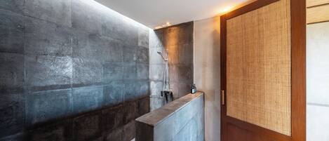 Un baño moderno con pared de piedra, puerta de madera con panel tejido y zona de ducha.