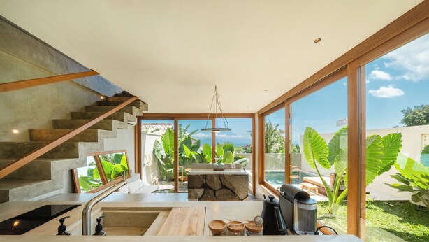 A modern kitchen with a stone island, stainless steel appliances, and large windows overlooking a garden. - Mizu Homes (Lembongan Island)