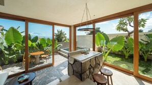A modern interior with large windows, a stone counter, and a view of a garden. - Mizu Homes (Lembongan Island)