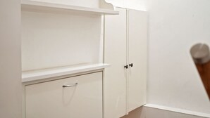 A white wardrobe with a handle, a shelf above it, and a door with a handle.