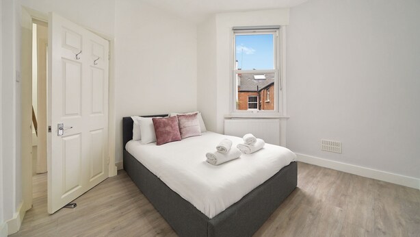 A bedroom with a bed, a window, a radiator, and a door.