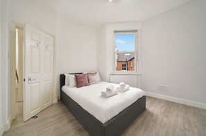 Un dormitorio con cama, ventana, radiador y puerta.