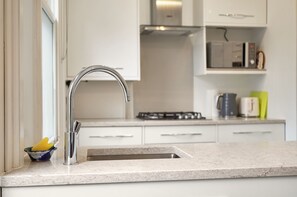 A kitchen with a stainless steel sink, white cabinets, a gas stove, and a microwave. - Bright and Relaxing London Base in Hampstead - Pass the Keys (London)