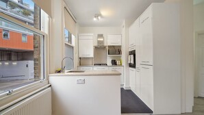 A modern kitchen with white cabinets, a built-in oven, and a window overlooking a building.