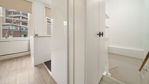A corridor with a radiator, a window with a view of buildings, and a door with a handle.