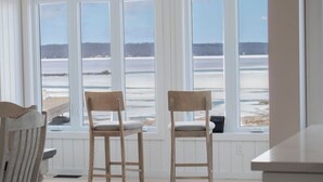 Een kamer met twee houten stoelen gericht op een groot raam met uitzicht op een strand.