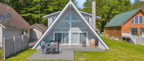 A modern house with a large deck, a covered grill, and a fenced backyard.