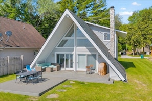 Ein modernes Haus mit Satteldach, einer Terrasse mit Gartenmöbeln und einem Steinkamin.