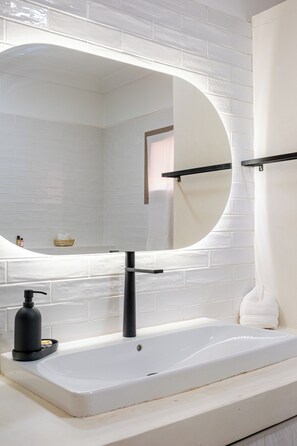 Ein Badezimmer mit einer weißen Badewanne, einem runden Spiegel und einer schwarzen Armatur.