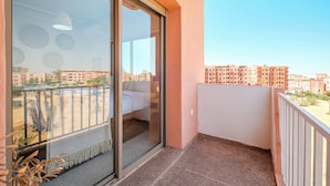 A balcony with a sliding glass door, a white sofa, and a view of a residential area with apartment buildings. - Majorelle Luxury Retreat Fully Equiped (Marrakech)