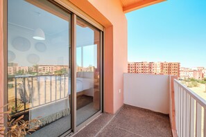Ein Balkon mit einer Schiebetür, einem weißen Sofa und Blick auf ein Wohngebiet mit Mehrfamilienhäusern.