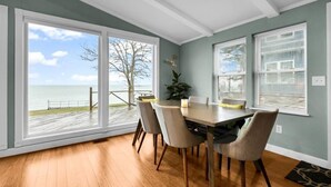 A dining area with a view of the ocean, a wooden deck, and a large window. - Panoramic Water Views (Lexington)