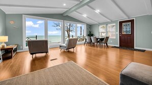 A spacious living room with a view of the ocean, wooden flooring, and a dining area with chairs and a table. - Panoramic Water Views (Lexington)