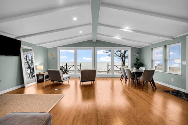 A spacious room with a large sliding glass door leading to a balcony, wooden flooring, and a dining area with chairs and a table.