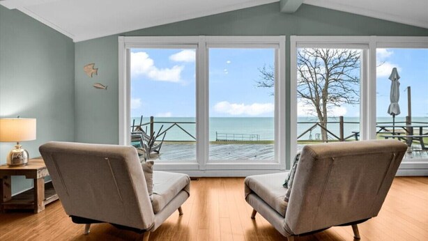 A room with two armchairs facing large windows overlooking a pier and the sea. - Panoramic Water Views (Lexington)
