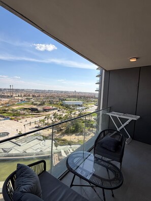 A balcony with a glass table and chairs, overlooking a cityscape with buildings and a park. - ELITE Iconic 3BR Apartment - ZED Towers (Sheikh Zayed City)