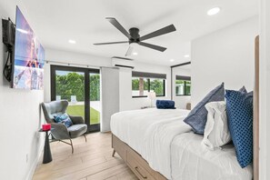 A modern bedroom with a bed, a chair, a ceiling fan, and a large window. - True Country/1 Acre/65ft Pool (Bermuda Dunes)