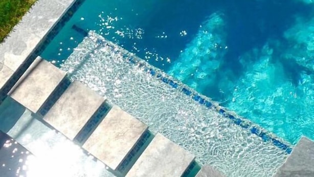 Une piscine à l’eau claire, des marches en pierre menant à l’intérieur de la piscine et une zone herbeuse à côté.