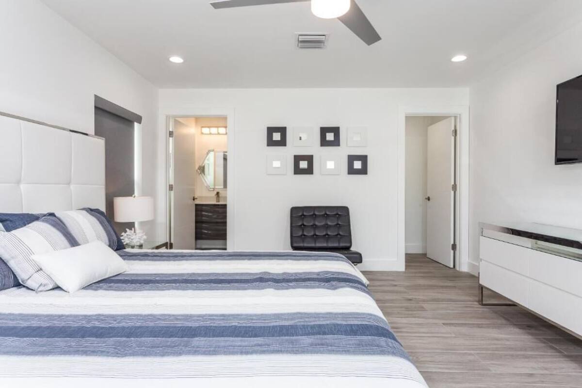 Een moderne slaapkamer met een groot bed, een plafondventilator, een inloopkast en een aan de muur bevestigde televisie.