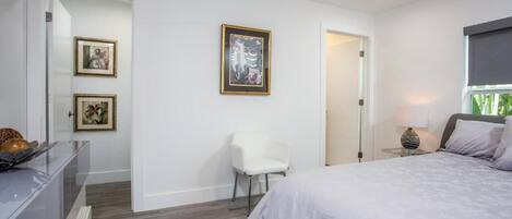 A modern bedroom with a bed, a chair, and framed artwork on the wall.