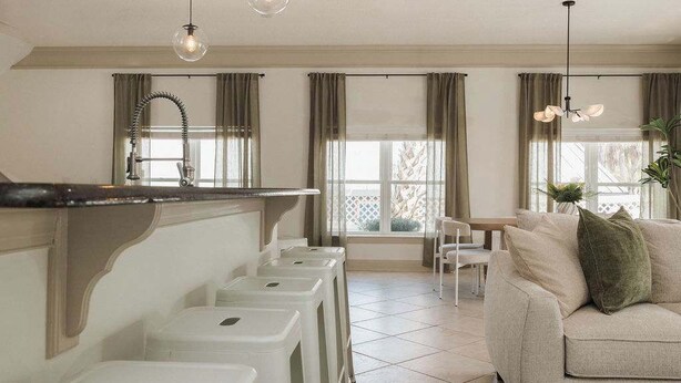 A kitchen with a sink, stools, and a dining area with a sofa and chairs. - Villa De Le Mar - Pool, Movie Theater (Jacksonville Beach)