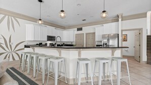 A modern kitchen with white cabinets, a central island with bar stools, stainless steel appliances, and pendant lighting. - Villa De Le Mar - Pool, Movie Theater (Jacksonville Beach)