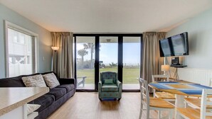 Een kamer met een bank, een stoel, een eettafel met stoelen, een televisie en uitzicht door een glazen deur.