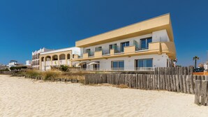 Een modern pand aan het strand met een meerlaags gebouw, een houten omheining en een zandstrand.