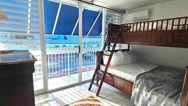 Ein Zimmer mit einem Etagenbett, einem Schreibtisch und einer großen Schiebeglasdoor zum Balkon.