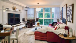 A modern living room with a flat-screen TV, a red sofa, a dining table with chairs, and a large window with natural light. - Prime Location in Condado Puerto Rico (San Juan)