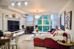 A modern living room with a flat-screen TV, a red sofa, a dining table with chairs, and a large window with natural light. - Prime Location in Condado Puerto Rico (San Juan)