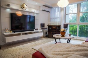 A modern living room with a large flat-screen TV, a fireplace, a dining area, and a large window with a view of trees. - Prime Location in Condado Puerto Rico (San Juan)