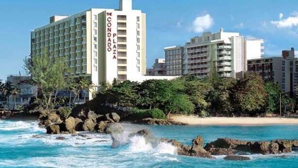 A coastal hotel with multiple floors, a visible name sign, and a beach in the background. - Prime Location in Condado Puerto Rico (San Juan)