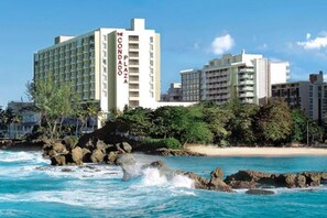 A coastal hotel with multiple floors, a visible name sign, and a beach in the background. - Prime Location in Condado Puerto Rico (San Juan)