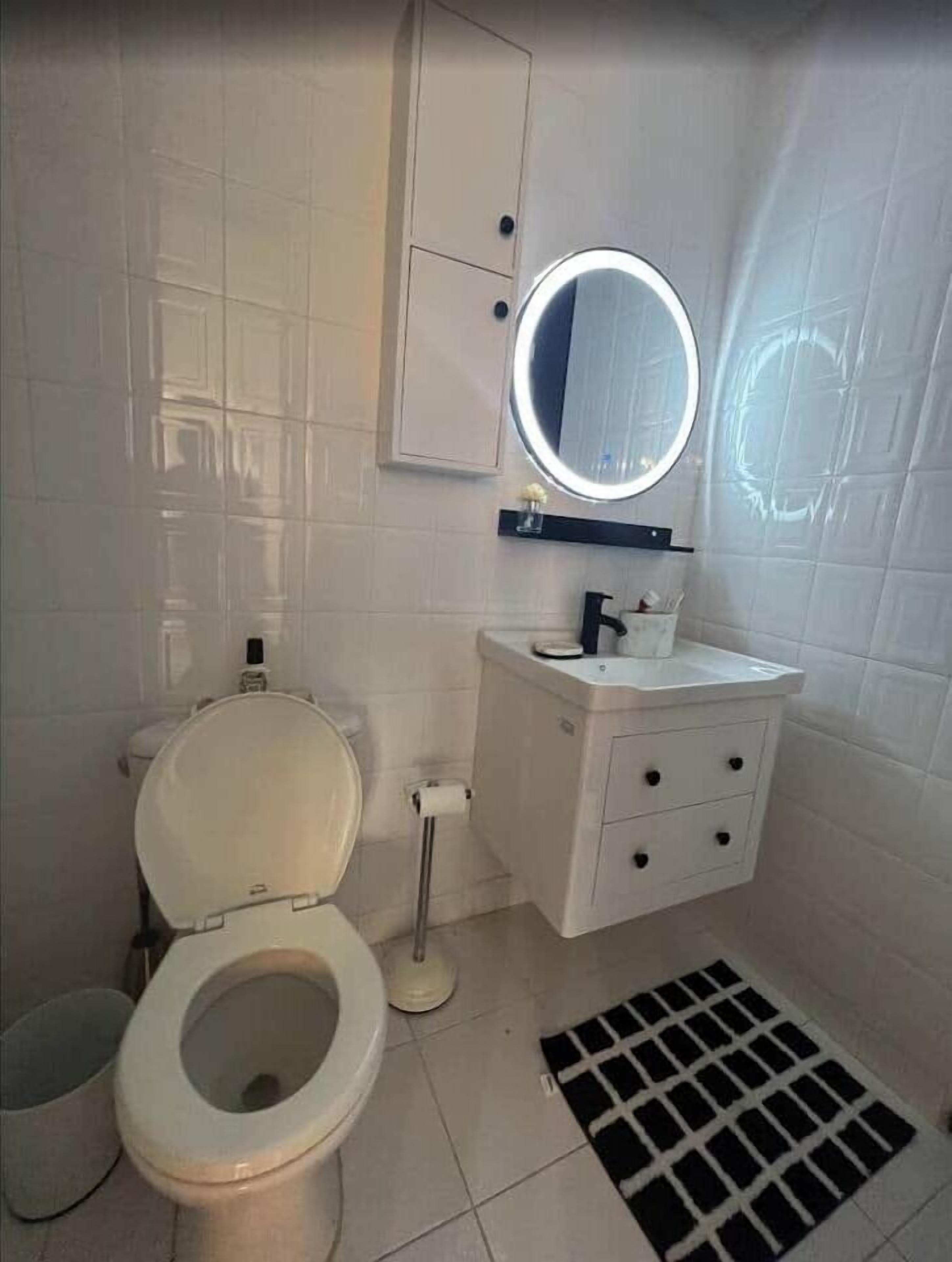 A bathroom with a toilet, sink, mirror, and a drain cover.