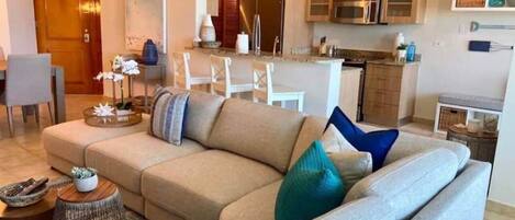 A living room with a sofa, coffee table, and a kitchen in the background.