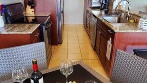 A kitchen with wooden cabinets, a refrigerator, a sink, and a dining area with a table set for wine tasting. - P1207-Oceanview Apartment- Peñamar (Fajardo)