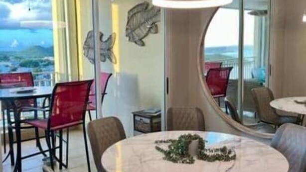 A dining area with a round table, chairs, and a view through glass doors. - P1207-Oceanview Apartment- Peñamar (Fajardo)