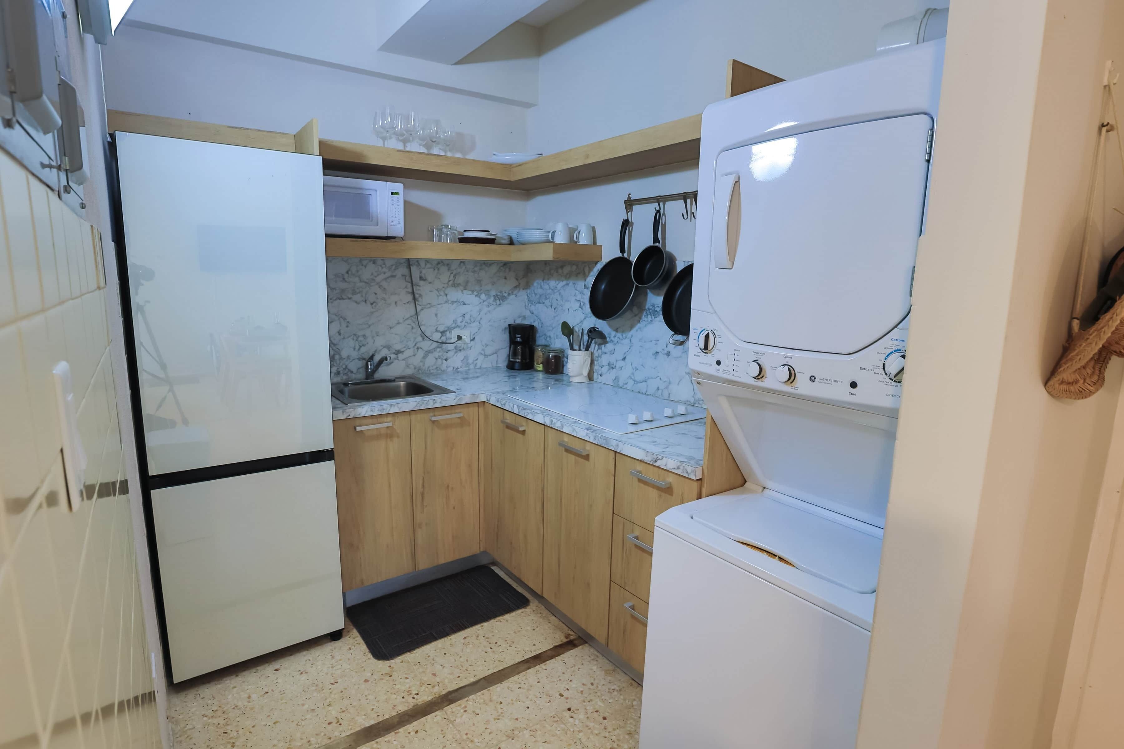 A compact kitchen with a refrigerator, microwave, and stacked washer-dryer unit.