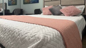Una cama con colcha, almohadas y cabecera en una habitación con cuadros en la pared.