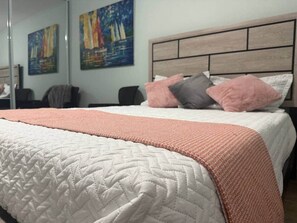 Ein Bett mit Tagesdecke, Kissen und einem Kopfteil in einem Raum mit Bildern an der Wand.