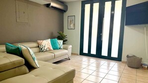 Una sala de estar con un sofá color beige, una planta y un ventanal corredizo.